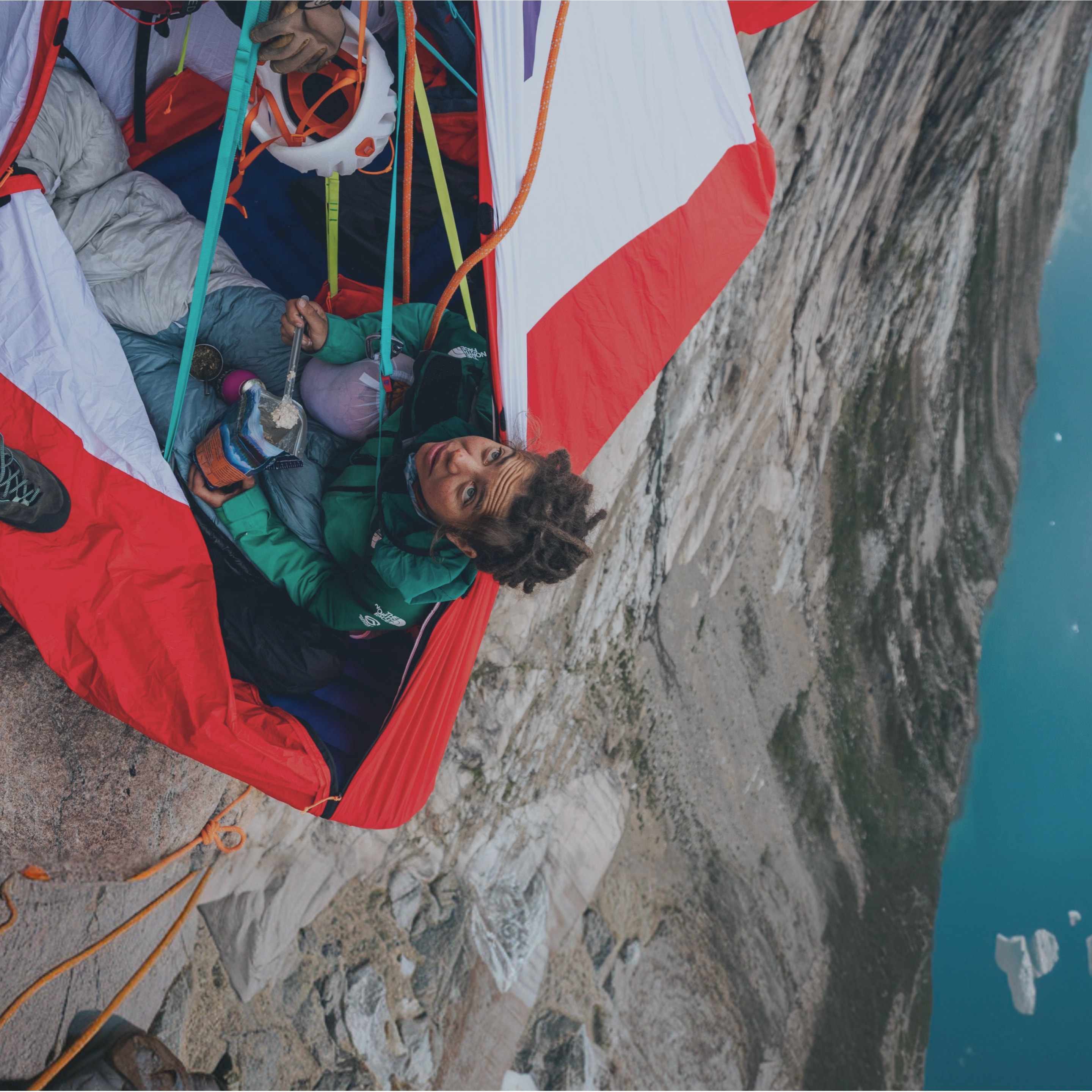 Climber eating a freeze-dried meal while resting in a portaledge suspended on a cliff face